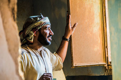 Smiling man looking away while standing by window of abandoned house