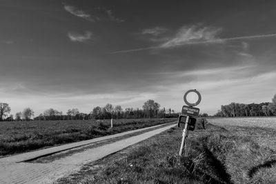 Road sign by railroad tracks on field against sky