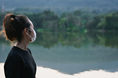 Side view young woman wear protection mask beside the lake and her look at faraway , hope and dream