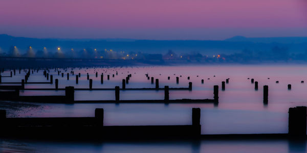 Silhouette wooden posts in lake against sky at sunset