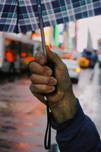 Cropped hand of man holding umbrella in city during rain