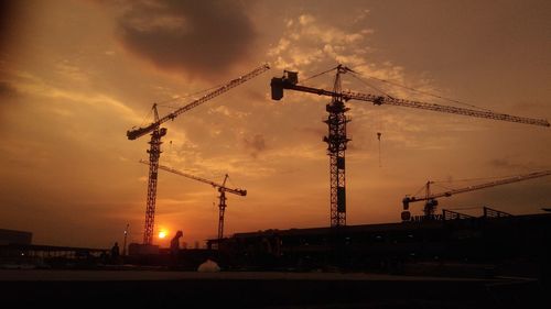 Silhouette cranes at construction site against sky during sunset