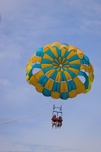 Low angle view of females paragliding against sky