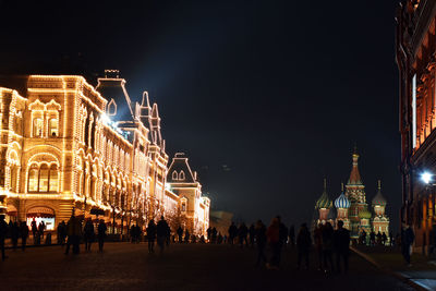 People at illuminated building against sky at night