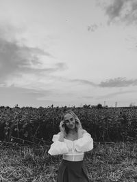 Portrait of young woman standing on field against sky