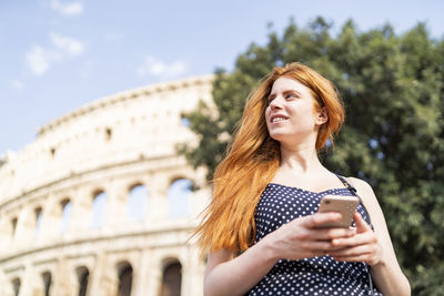 Smiling female tourist with smartphone on sunny day near attraction