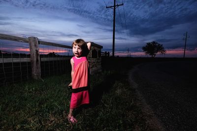 Young woman standing on grass against sky