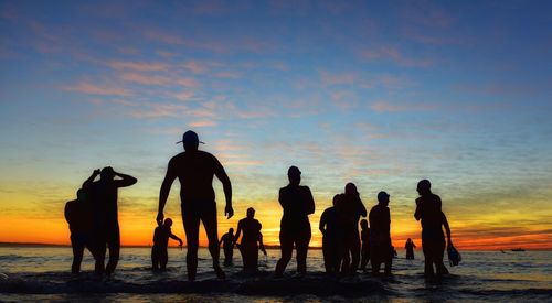 Silhouette people enjoying in sea against sky during sunrise