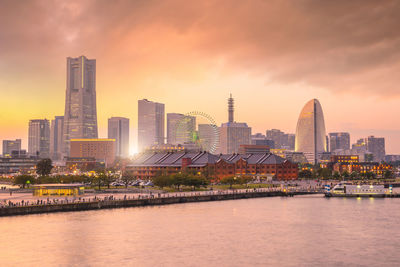 River by buildings against sky during sunset