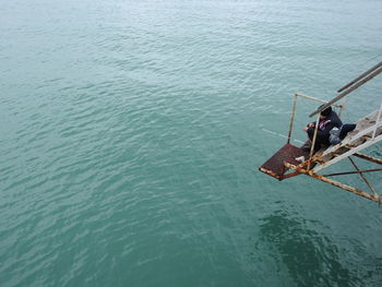 High angle view of man fishing while sitting on staircase by sea