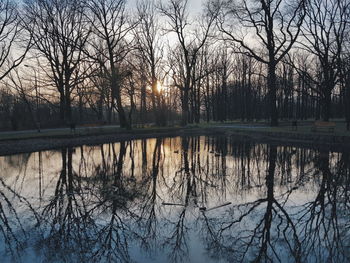 Silhouette bare trees by lake against sky during sunset