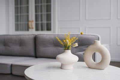 Modern ceramic vases with bouquets of mimosa flowers on a coffee table in the living room
