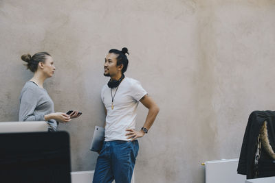 Male and female computer programmers discussing against wall in office