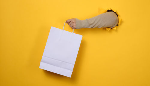 Female hand holds a white paper disposable bag with handles for groceries and clothes. 