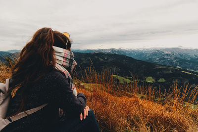 Side view of woman looking at mountains against cloudy sky