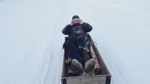 High angle view of woman lying in sled on snow covered field