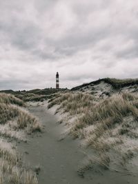 Scenic view of beach and lighthouse against cloudy sky