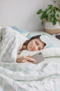 Tired woman using smart phone lying on bed