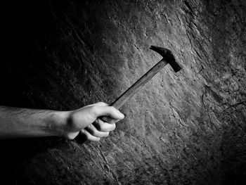 Cropped hand of man holding hammer against wall