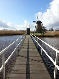 Empty footbridge over river against sky