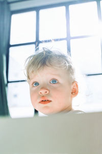 Portrait of cute boy looking through window at home