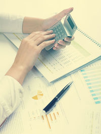 Cropped hands of businesswoman using calculator with documents at desk