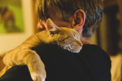 A red sleeping cat lies on the shoulder of a blond man