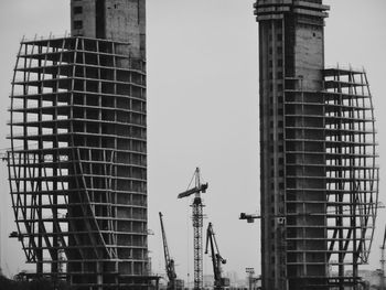 Cranes by incomplete building against sky