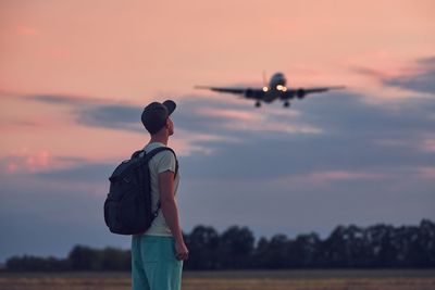 Rear view of man standing on airplane against sky during sunset