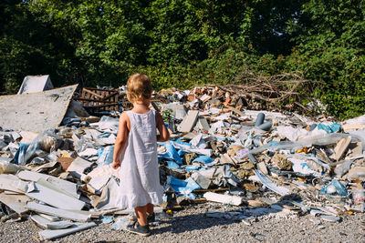 Little girl at a dump among a heap of scattered garbage in the forest.