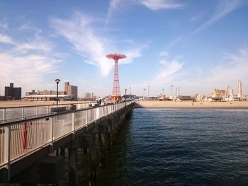 Pier over sea by parachute jump against sky