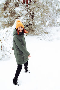 Cheerful girl in warm clothes playing with snow outdoors near the beautiful forest