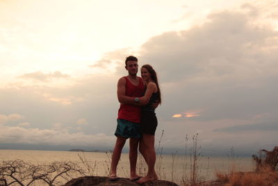 Portrait of couple standing on beach against sky during sunset