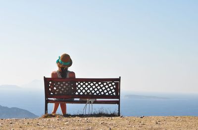 Rear view of woman sitting on bench at observation point