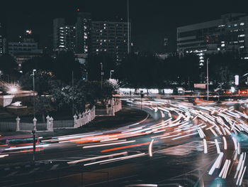 Light trails on road by buildings in city at night