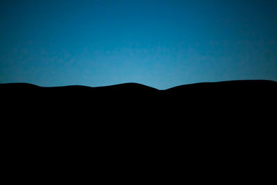 Silhouette mountain against clear blue sky at night