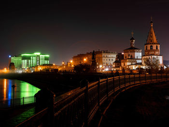 Illuminated bridge by buildings against sky at night