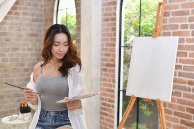 Young woman holding colorful palate against brick wall