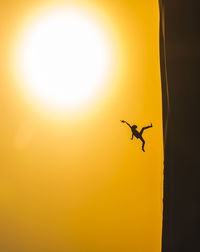 Tilt shot of silhouette person jumping over sand dune at desert against orange sky during sunset