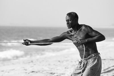 Full length of shirtless man at beach against sky