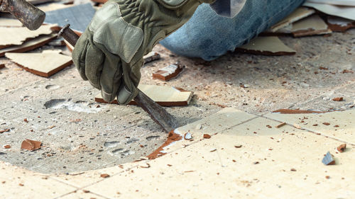 Cropped hand of manual worker removing tile from floor