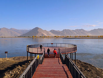 Rear view of men on pier over lake against sky