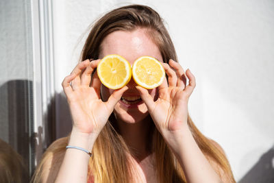 Close-up of smiling young woman holding lemon against wall