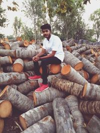 Full length of young man sitting on stack of logs