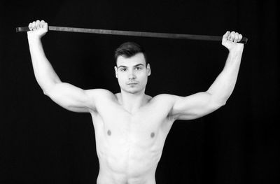 Portrait of shirtless young man holding equipment against black background
