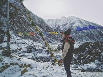 Side view of man standing by prayer flags on snow covered mountain