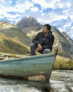 Man sitting on lake against mountains