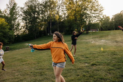 Smiling girl spraying water on friends while playing on grass in playground