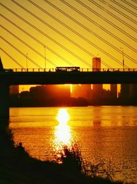 Silhouette bridge over river against sky during sunset