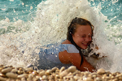 Close-up of smiling woman splashing water in sea